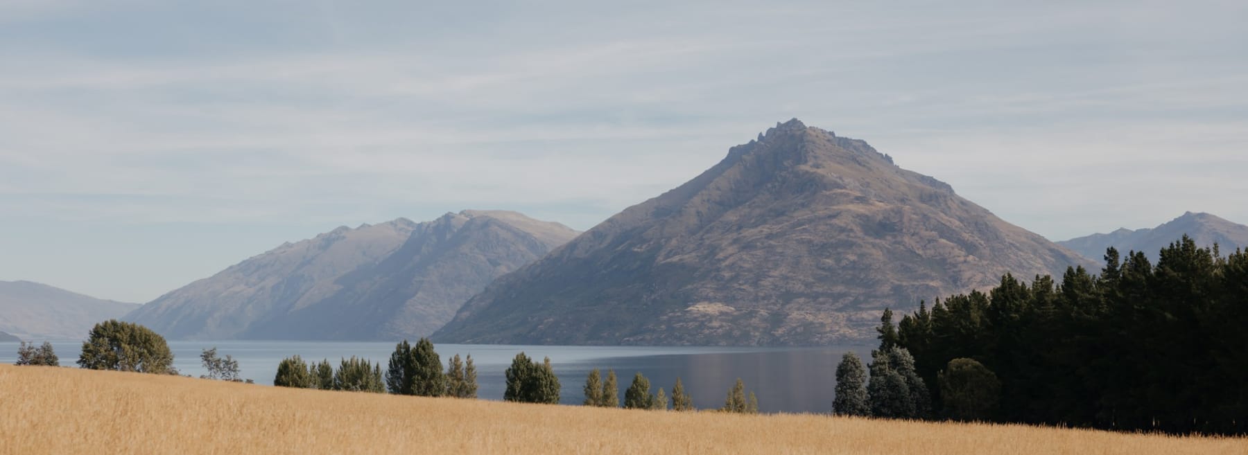 Golden fields running down to a deep blue lake, with a steep mountain behind it
